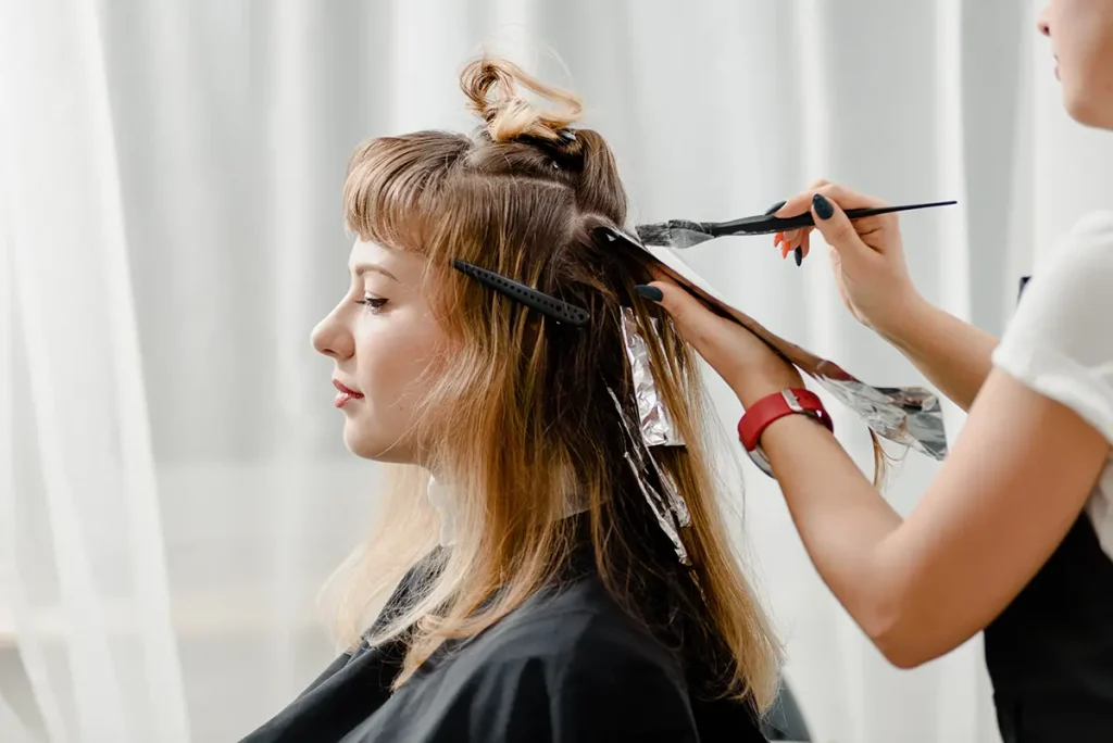 A side view of a woman getting her hair dyed, the stylist is putting foils in her hair.