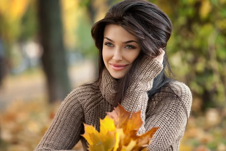 Girl with dark hair wearing a sweater and holding fall leaves